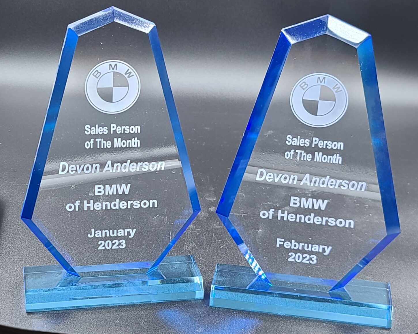 Two blue-tinted crystal glass awards with engraved BMW logo and salesperson of the month recognition