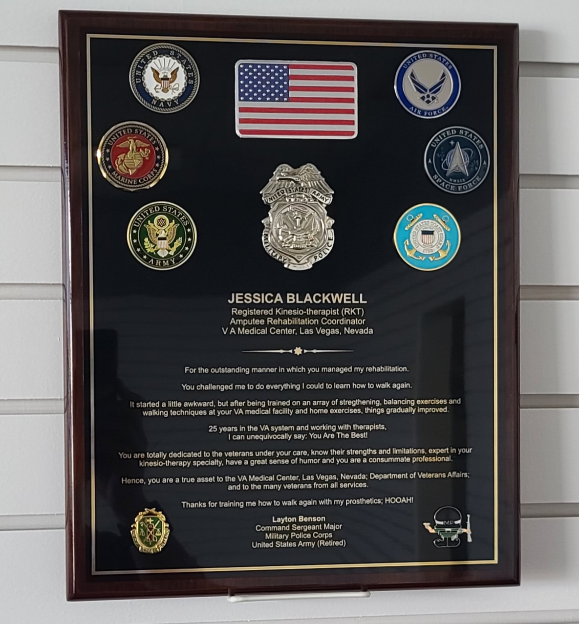 Framed military recognition plaque with branch coins, American flag, police badge, and engraved tribute letter on black background