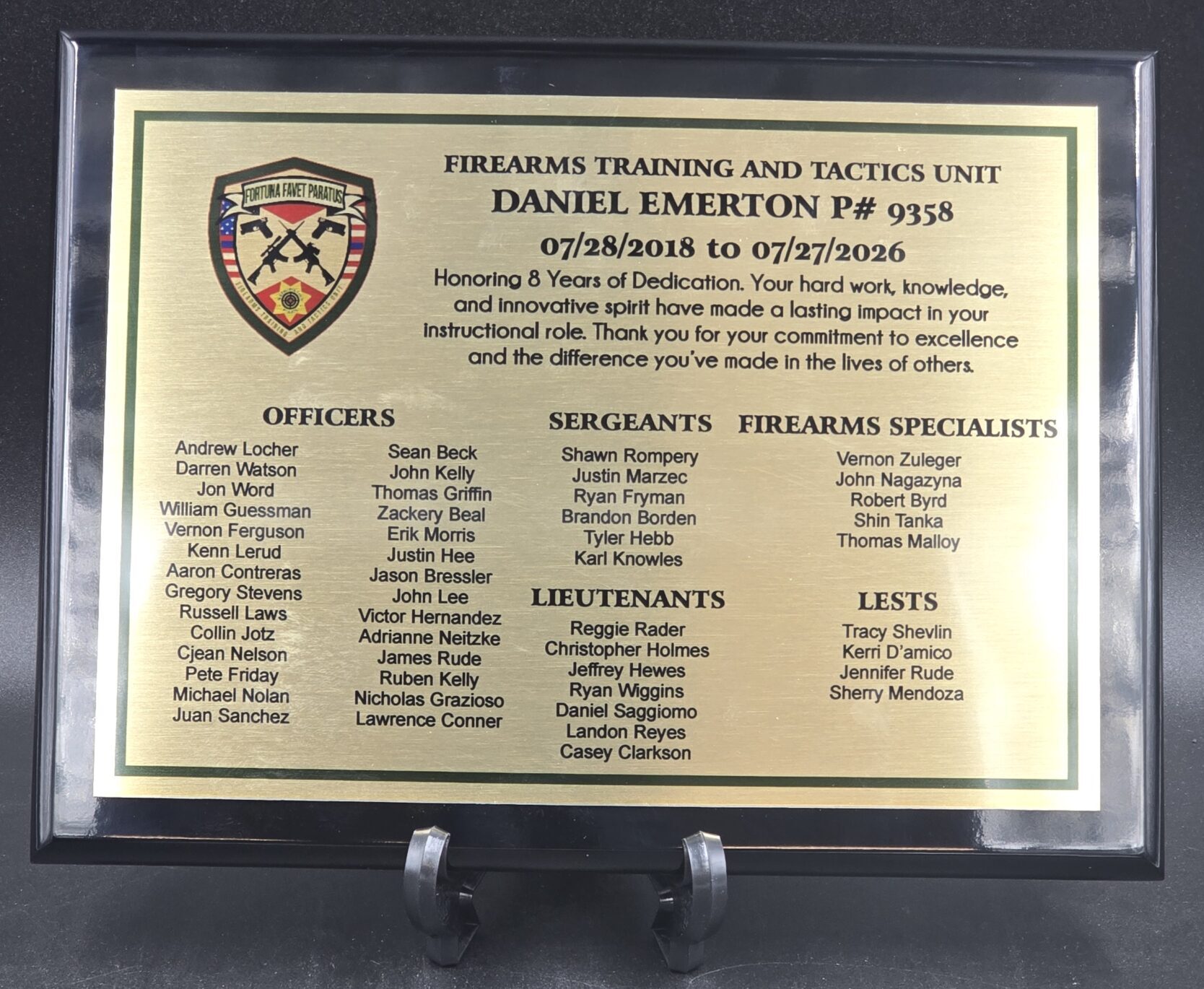 Black framed gold engraved plaque honoring 8 years of service with firearms training unit and staff names